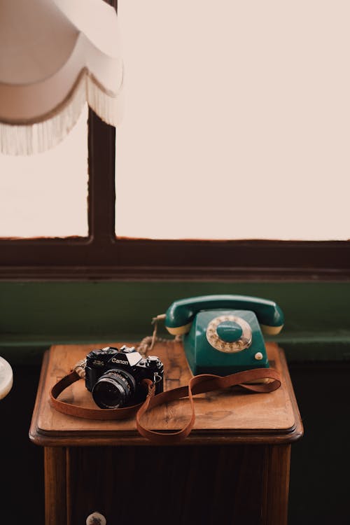 Retro photo camera and vintage telephone placed on wooden bedside table