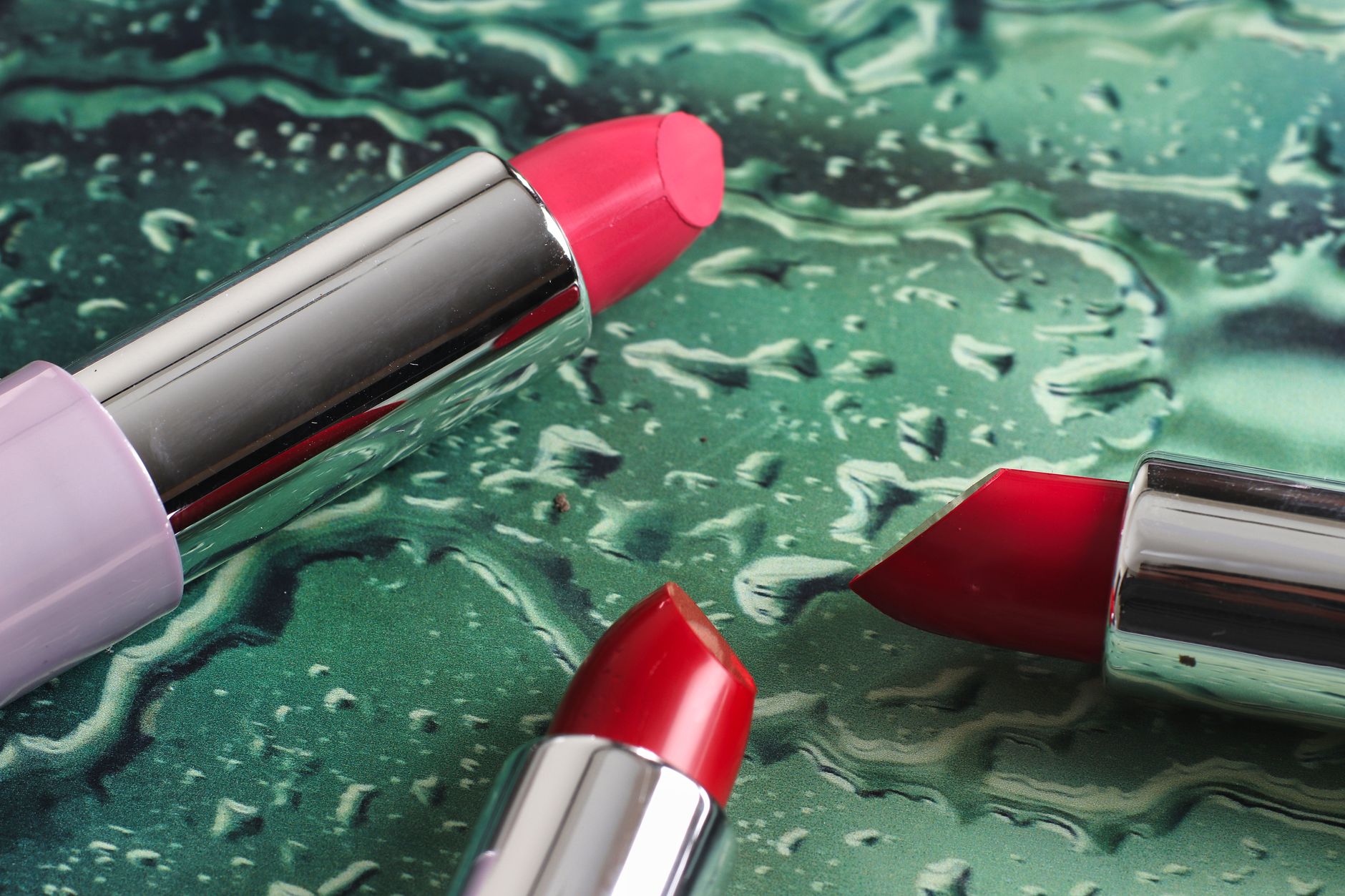 Close-up of colorful lipsticks on a textured, wet surface showcasing makeup beauty.