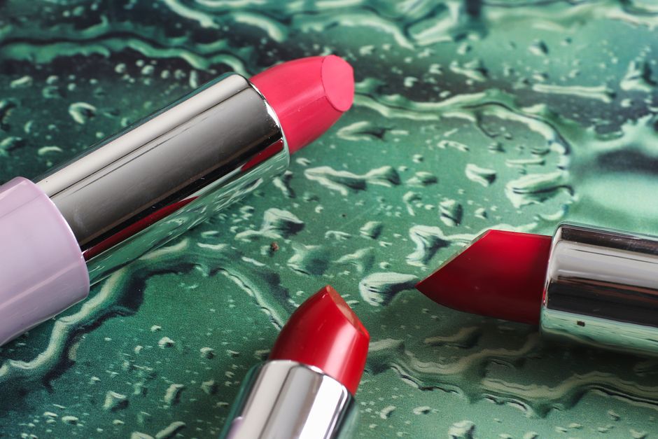 Close-up of colorful lipsticks on a textured, wet surface showcasing makeup beauty.