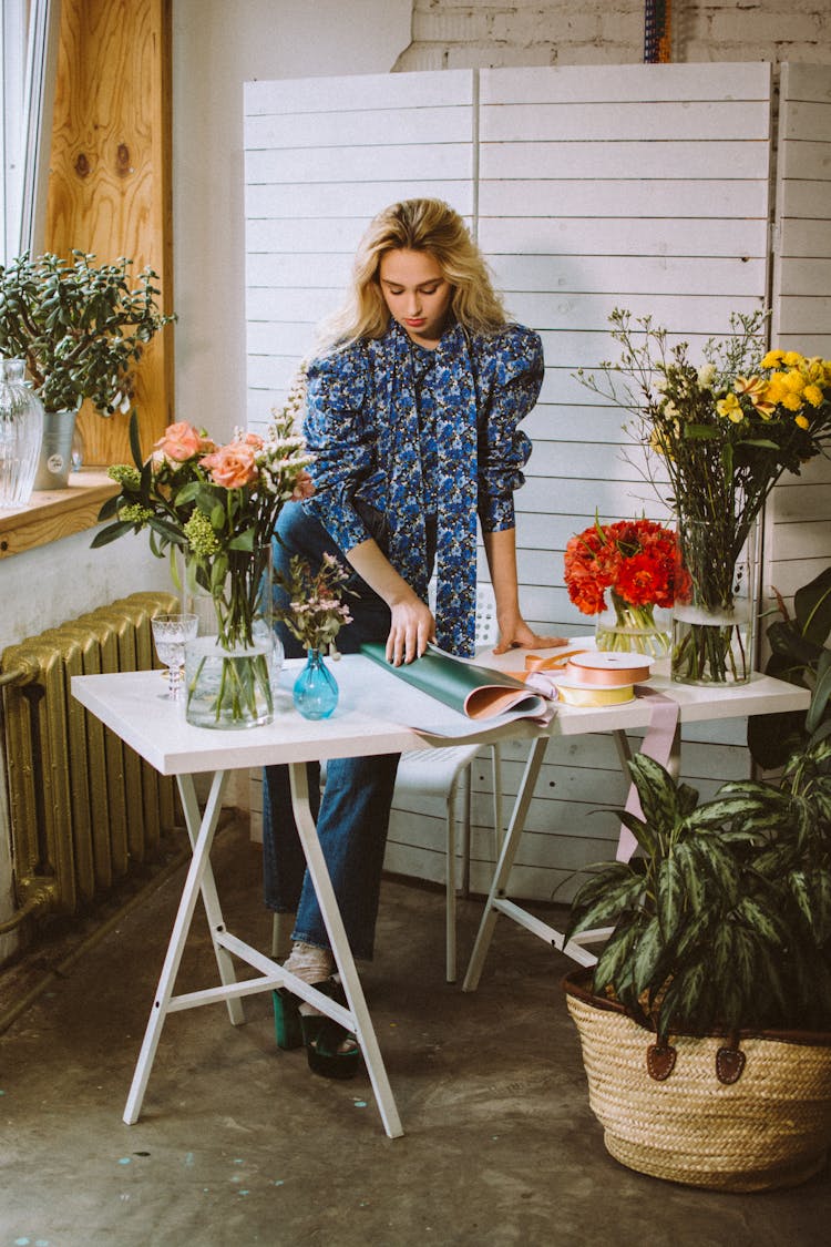 Florist At Table With Wrapping Paper And Flowers