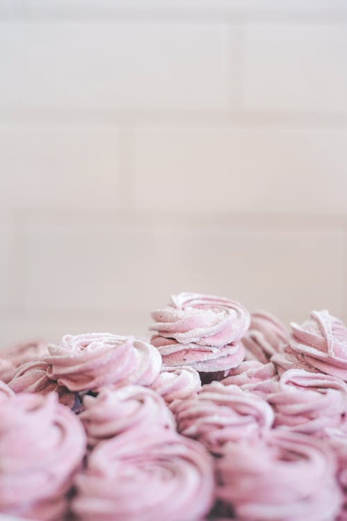 Pile of delicious sweet pink zefir sprinkled with white powdered sugar served in light room on white background at home