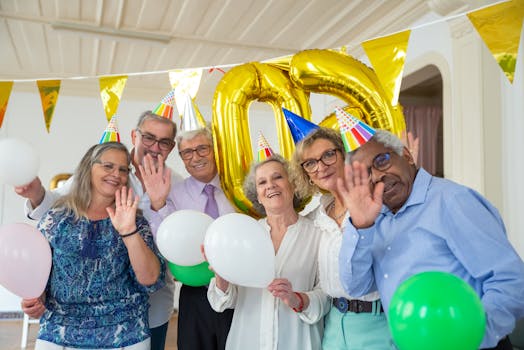 Joyful elderly group celebrating a birthday with balloons and party hats indoors.