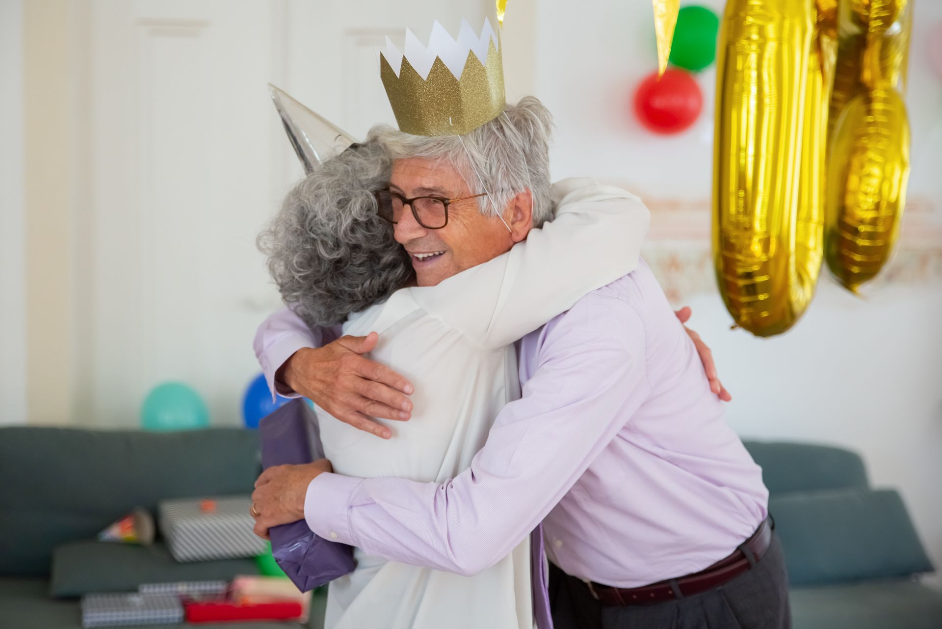 Heartwarming scene of a senior couple hugging at an indoor birthday party with colorful decorations.