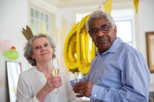 Free An elderly couple enjoying a festive celebration at home, holding champagne glasses with decorations in the background. Stock Photo