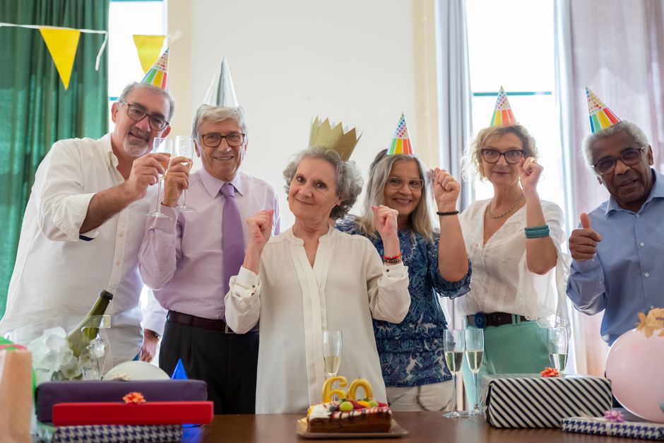 personalized gifts for grandparents - Group of seniors joyfully celebrating a birthday with party hats and cake indoors.