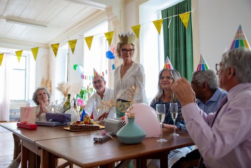 Free A joyful birthday party with mature friends celebrating indoors with decorations and wine. Stock Photo