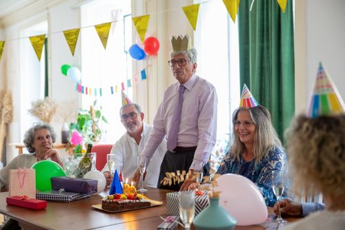 Free Smiling seniors celebrating a birthday party indoors with decorations and cake. Stock Photo