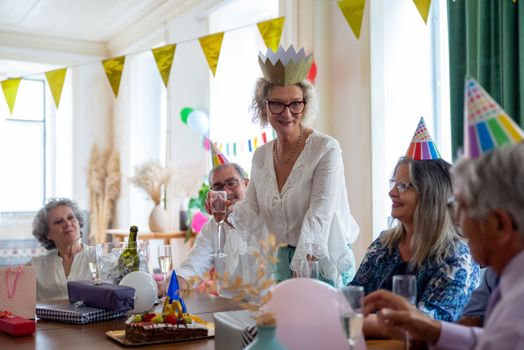 Joyful group of seniors celebrating a birthday party indoors with hats and drinks.