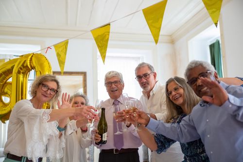 Free Lively group of mature friends celebrating with champagne indoors, waving happily. Stock Photo