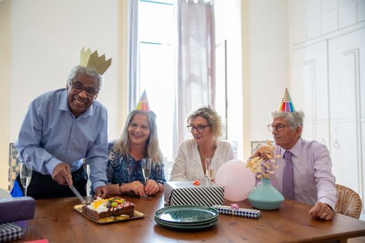 Senior friends enjoying a birthday celebration indoors, with cake and party hats.