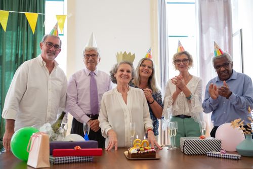 Free A group of seniors celebrate a birthday indoors with smiles, cake, and party hats. Stock Photo