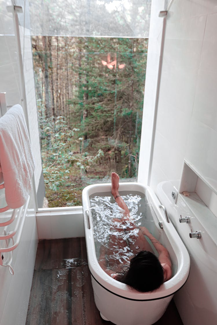 A Person Relaxing On A Bath Tub While Looking At The Beautiful Scenery From The Glass Window