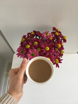 A soothing top view of a hand holding a coffee cup with vibrant flowers in the background.
