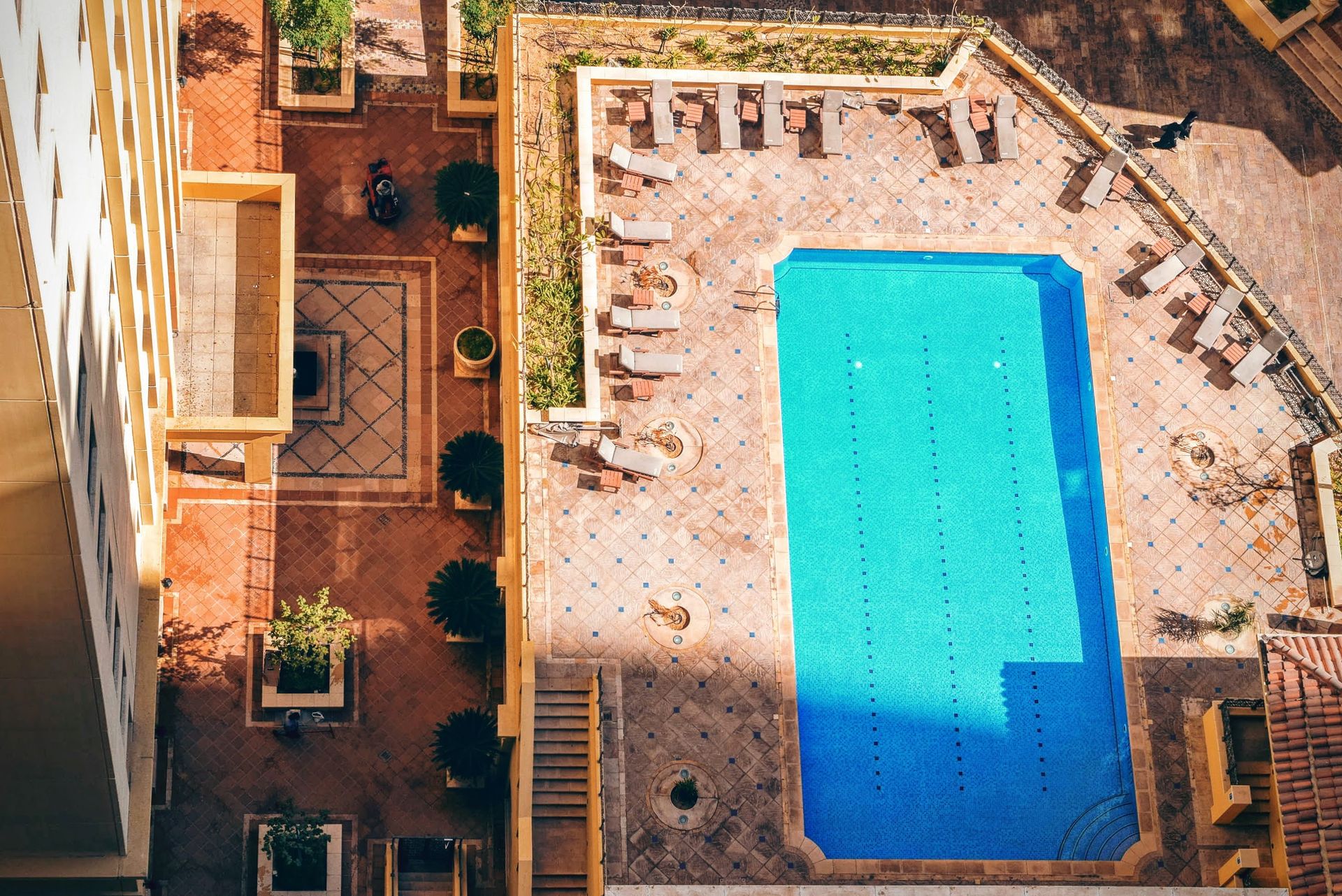 Aerial view of a luxurious hotel pool with sunlit surrounding seating and patio.