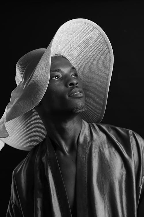 Black and white of African American female model wearing shirt and trendy headwear standing on black background in modern studio