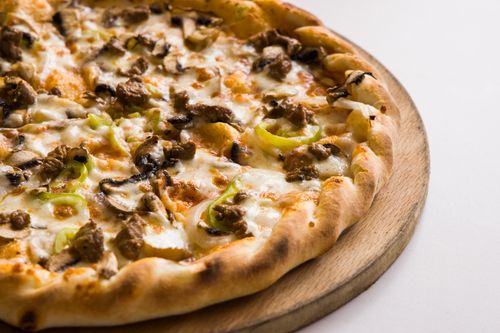 Free Close-up of a cheesy pizza topped with mushrooms and green peppers on a wooden board. Stock Photo