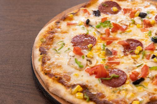 Free Close-up of a tasty pepperoni pizza with vegetables, cheese, and mushrooms on a wooden board. Stock Photo