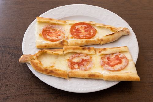 Free Top view of Turkish pide with cheese and sliced tomato on a white plate, perfect for food photography. Stock Photo