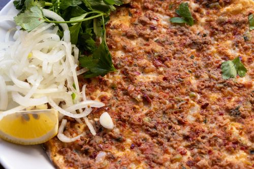 Free Close-up of a traditional Turkish lahmacun topped with minced meat, onions, parsley, and lemon slices. Stock Photo