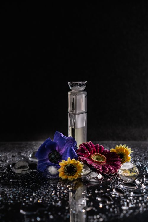 Free A captivating still life featuring a perfume bottle surrounded by vibrant flowers and glistening water droplets. Stock Photo