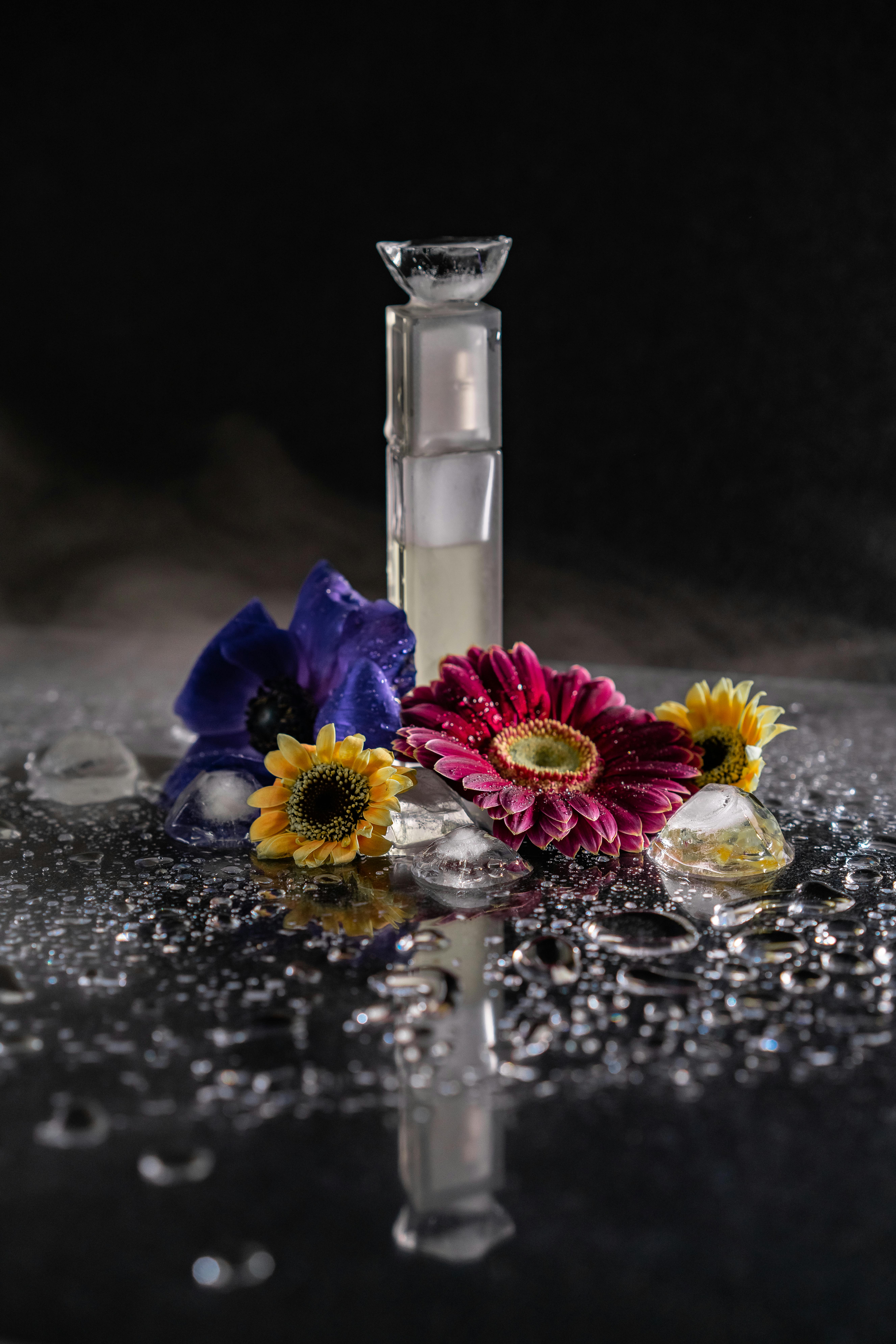 Perfume bottle surrounded by vibrant flowers and reflections with water droplets.