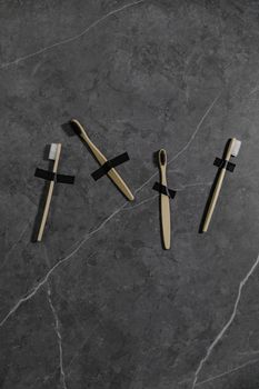 Minimalist composition of four bamboo toothbrushes taped to a dark marble surface, promoting sustainable dental care.