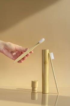 Hand holding a bamboo toothbrush with dental hygiene products on a beige background.