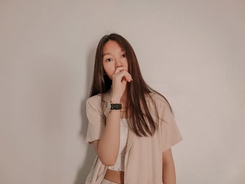 Free Young woman in casual outfit stands against a plain white wall, looking thoughtful. Stock Photo