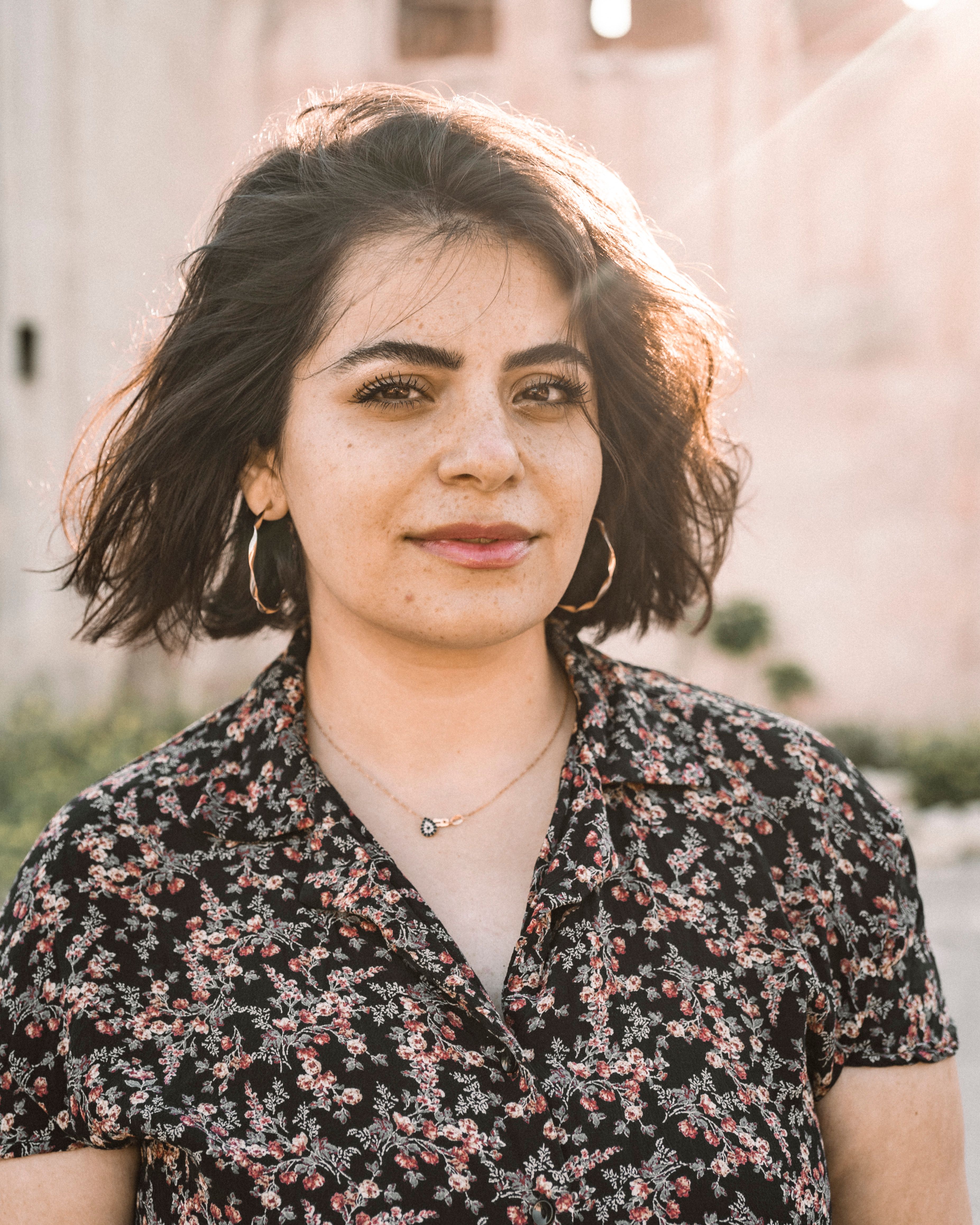 A woman wearing floral attire poses outdoors, captured in Gaziantep, Turkey under natural sunlight.