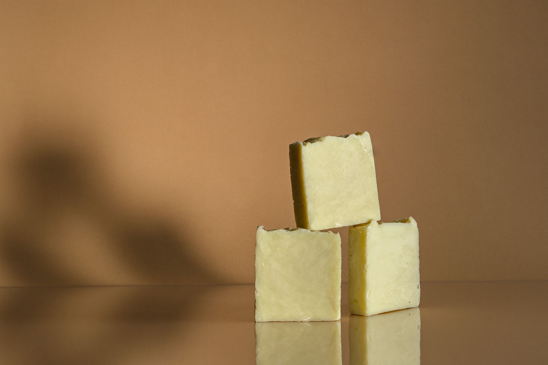Three handmade soap bars artfully stacked on a reflective surface with neutral background.