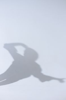Shadow art of a person posing against a white wall, creating an abstract and conceptual visual.