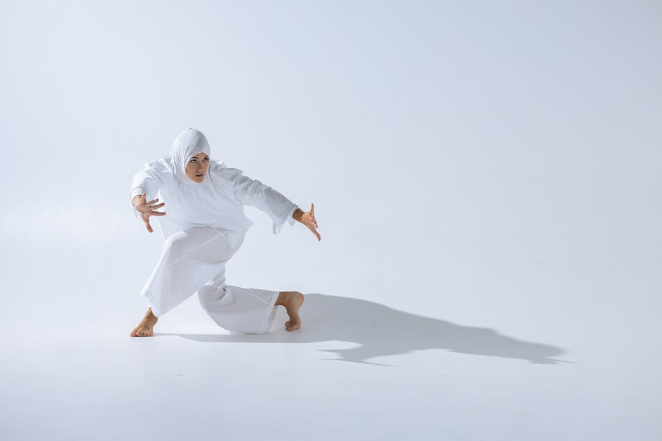 A Muslim woman gracefully performs a dance in a white studio setting, creating dramatic shadows.