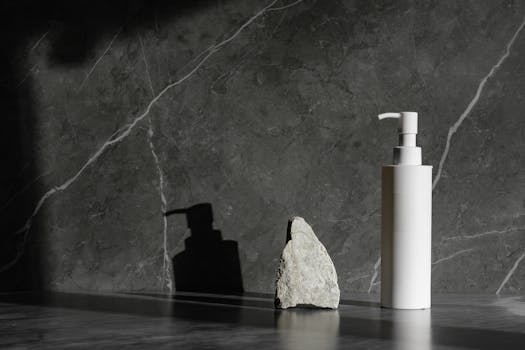 Sleek white pump bottle beside a rock on a marble surface with dramatic lighting.