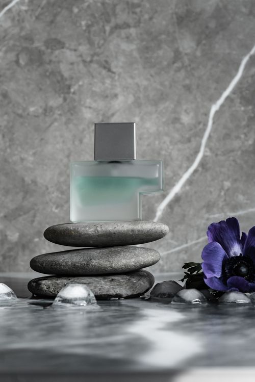 Free Stylish perfume bottle on stacked stones with floral accent against a marble backdrop. Stock Photo
