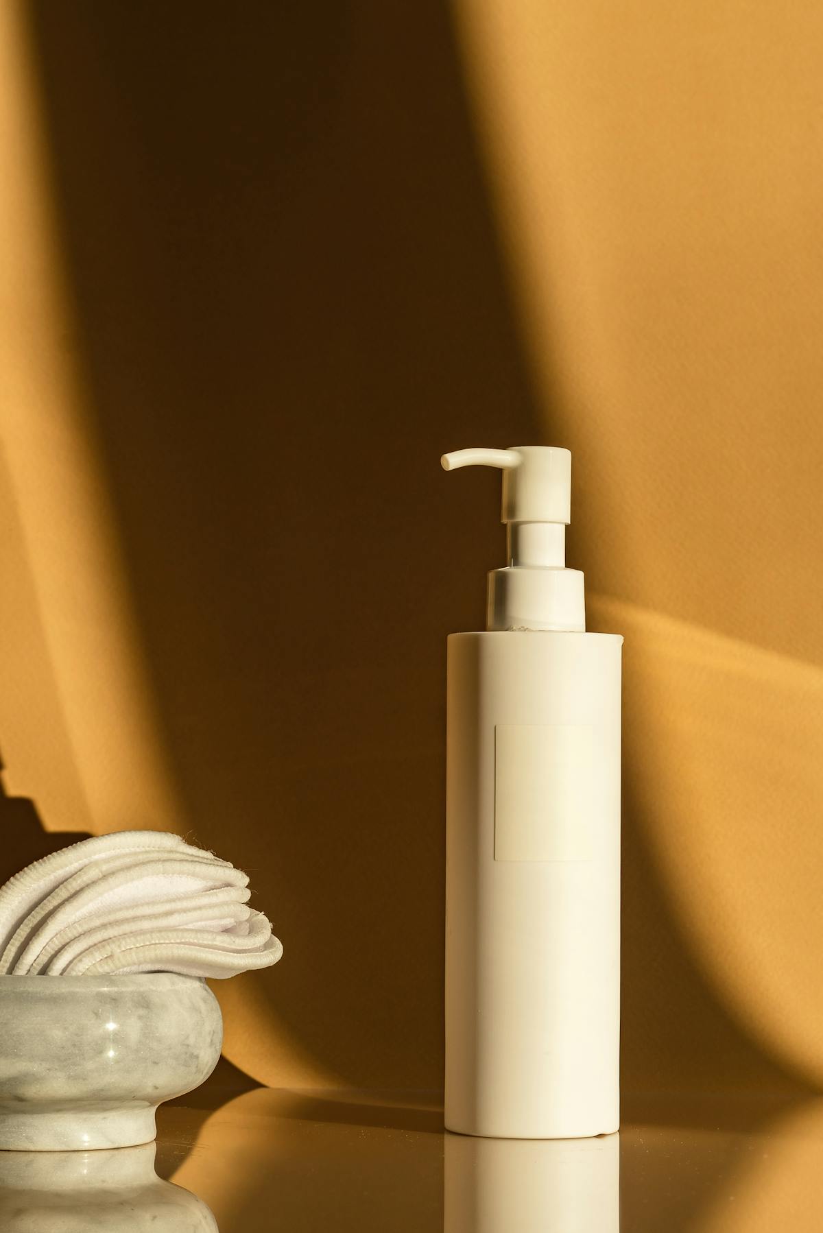Bottiglia cosmetica bianca con erogatore a pompa su sfondo beige caldo