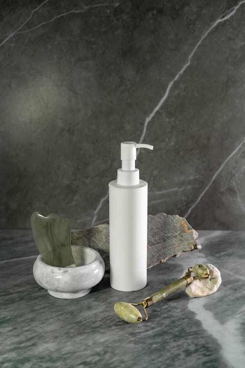 Dispenser Bottle With Gua Sha and Jade Roller On Marble Surface