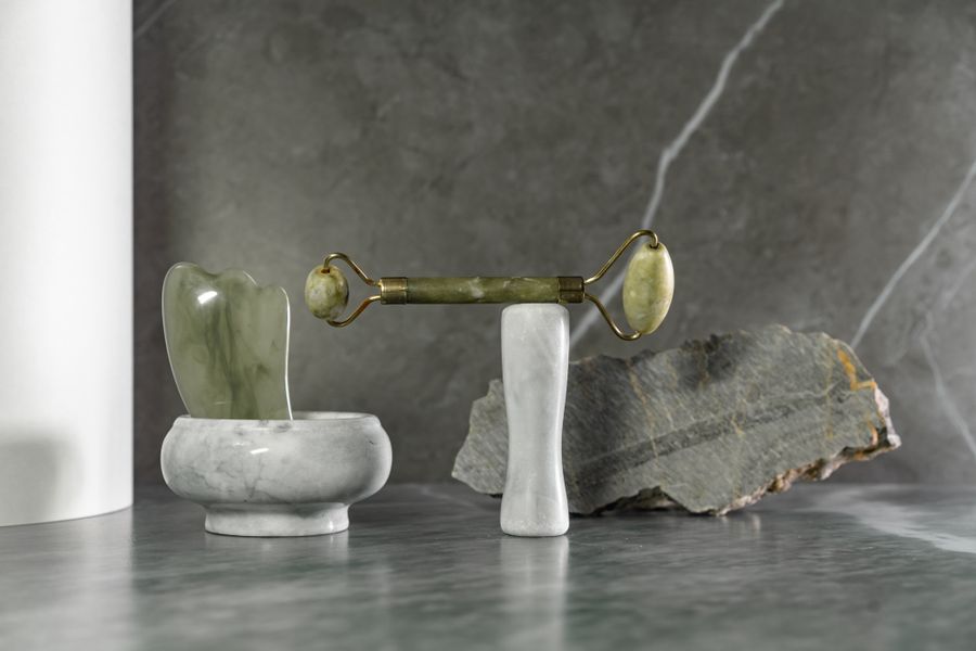 Green jade roller and gua sha stone on a marble surface