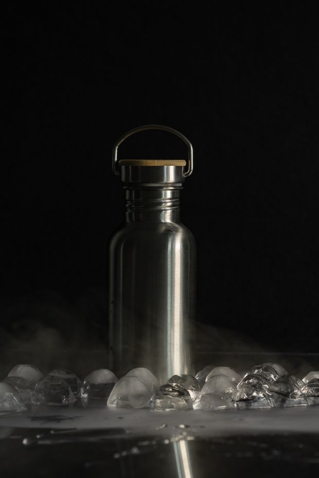 Stainless steel flask surrounded by ice on a dark surface, photo by Mikhail Nilov on Pexels