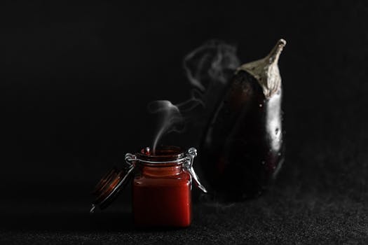 A minimalistic composition featuring an eggplant and a steaming jar against a dark backdrop.