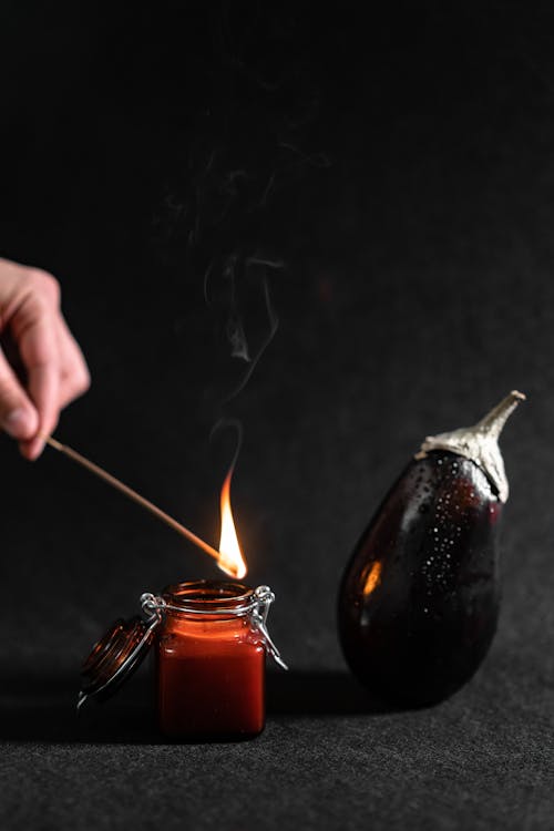 Person Lighting A Scented Candle Beside An Eggplant