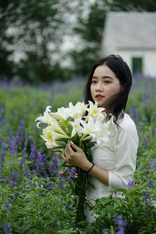 Free Charming Asian female with long hair standing in blooming meadow with bouquet of fresh Easter lilies Stock Photo