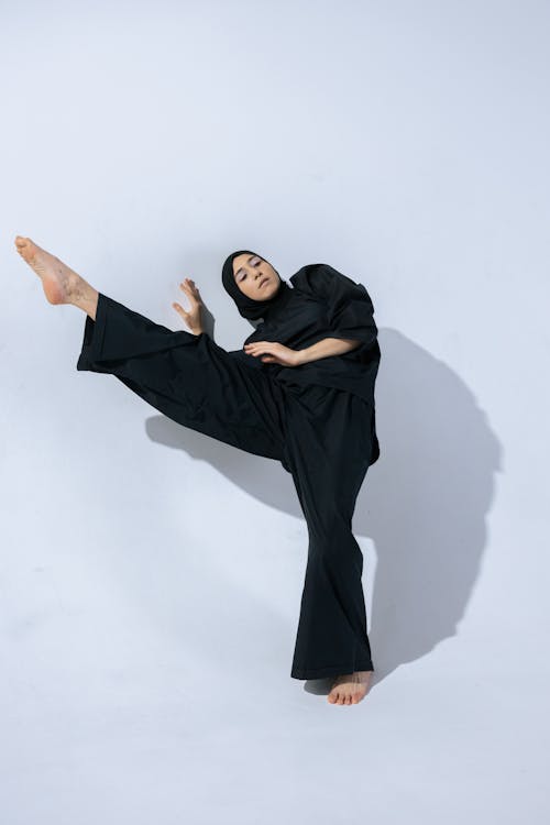 Woman in Black Hijab and Abaya Standing Beside a White Wall