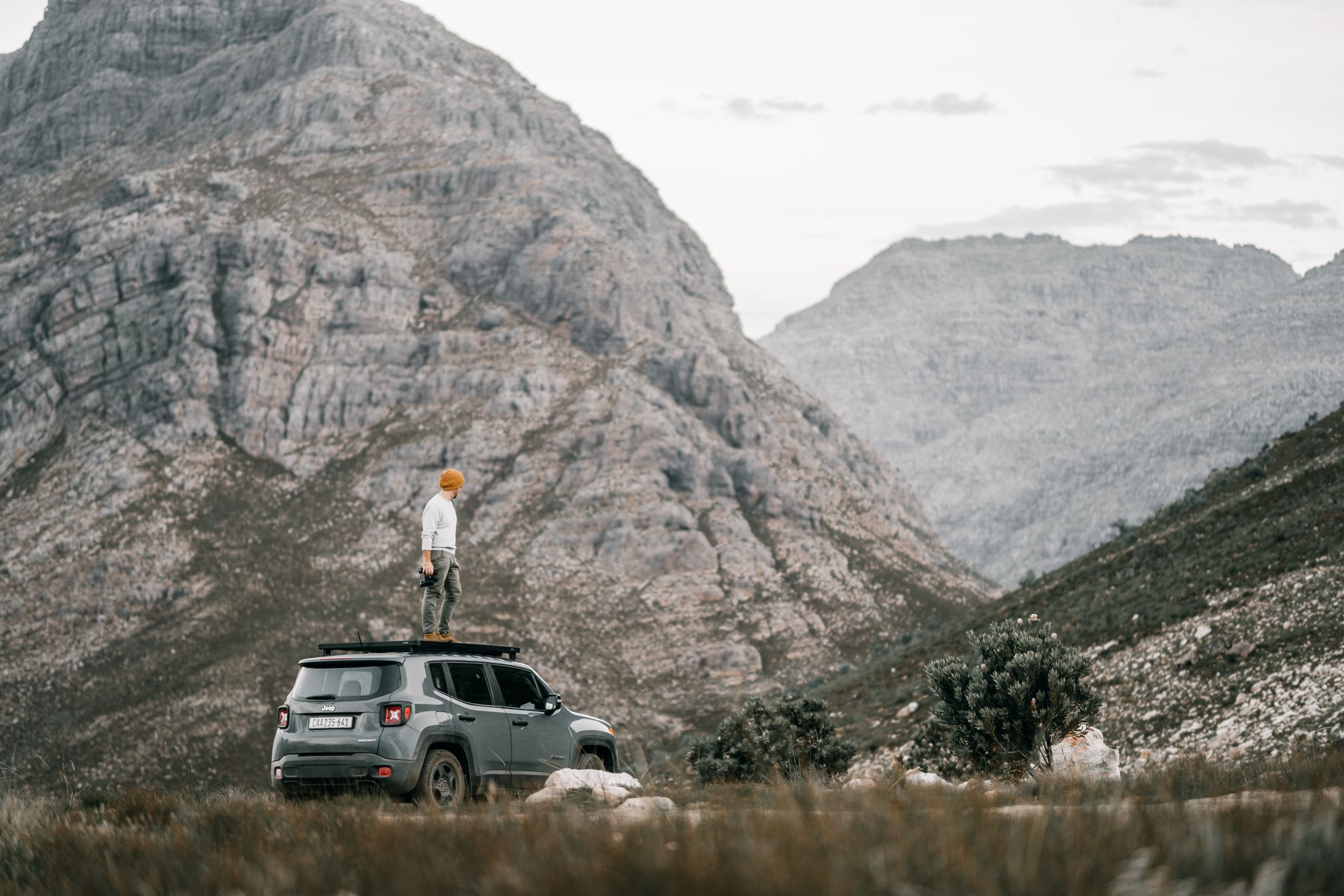 A person stands atop an SUV amidst a stunning mountainous landscape, embodying travel and exploration.