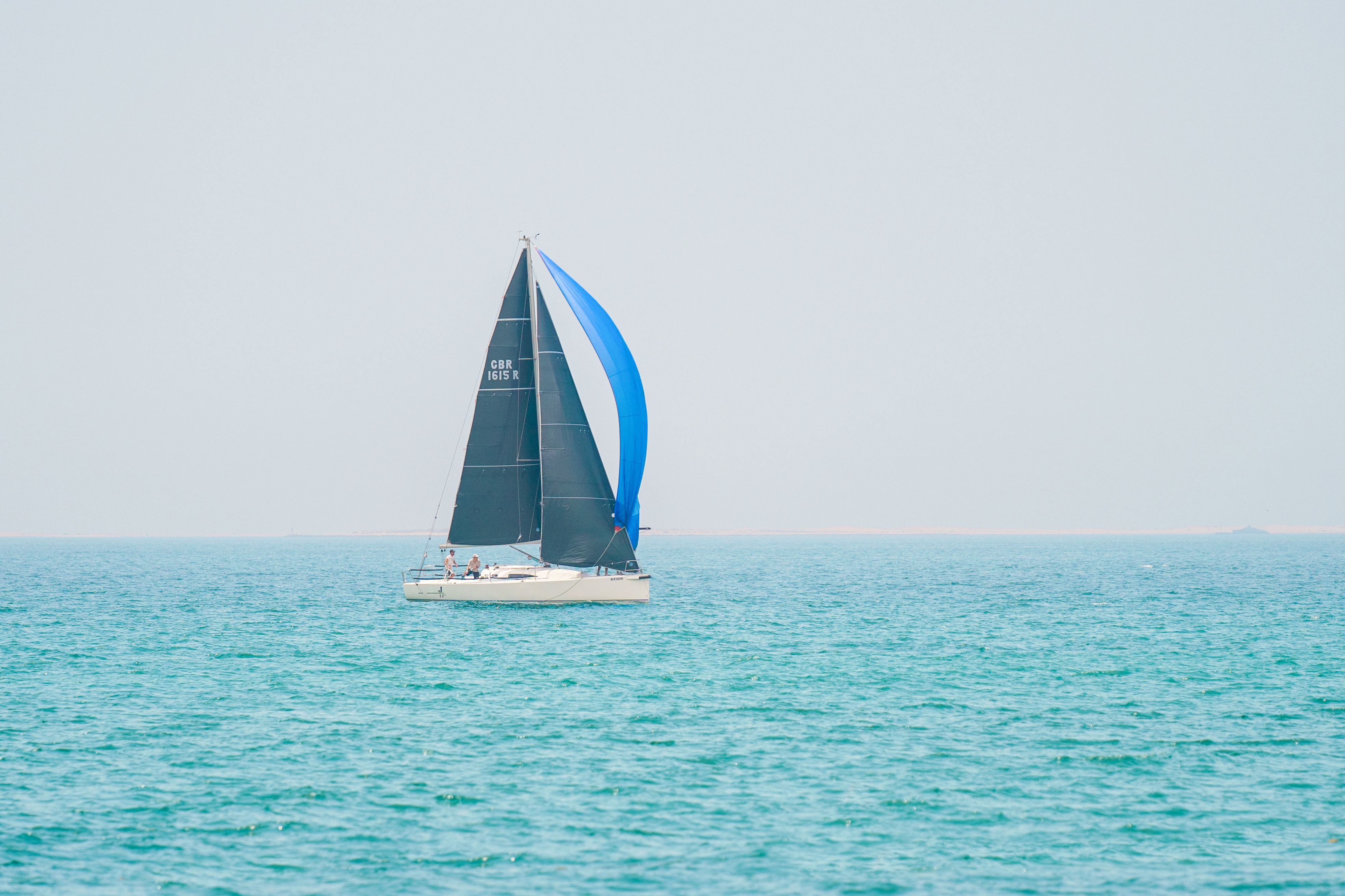 Incredible Luxury Shared Yacht Tour in Dubai Marina with Food Review 2026 - A sailboat with a blue and black sail glides on turquoise waters in Dubai.
