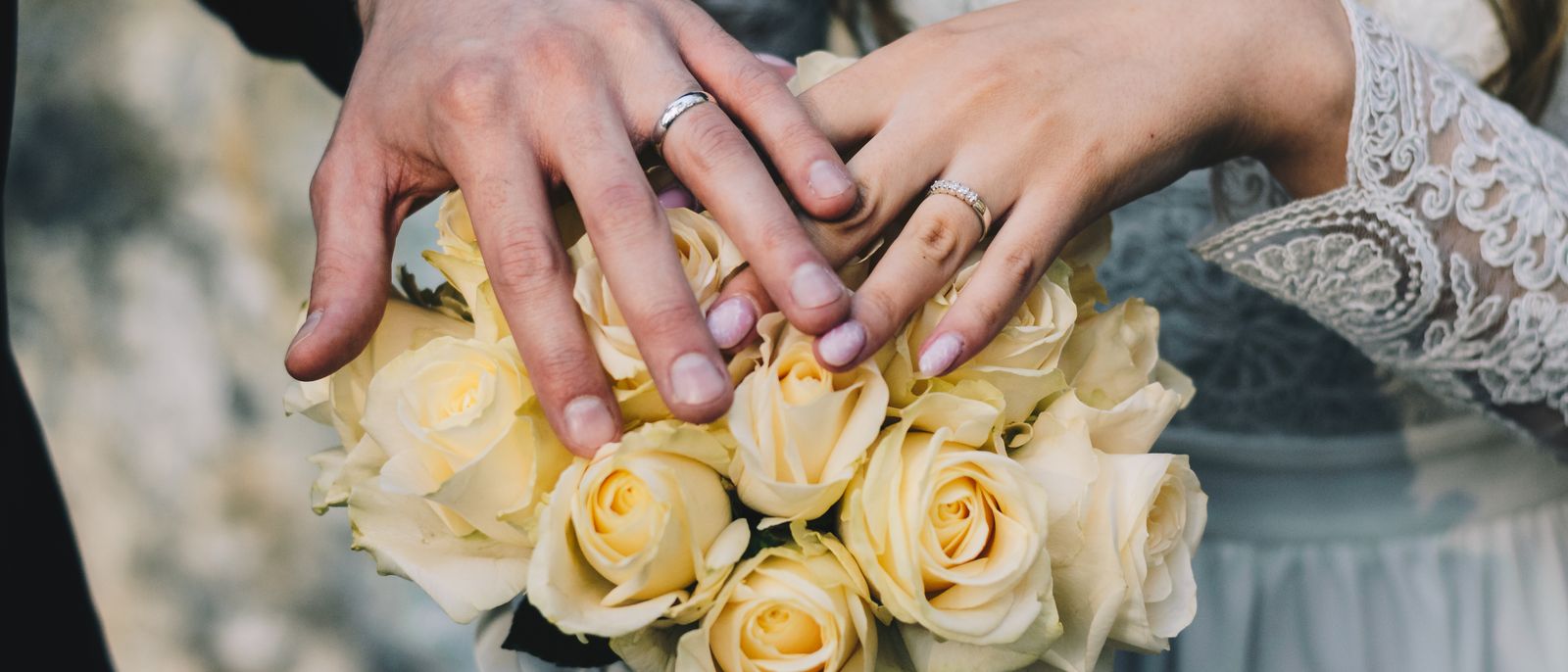 Close-up of a couple's hands displaying wedding rings above a bouquet of yellow roses.