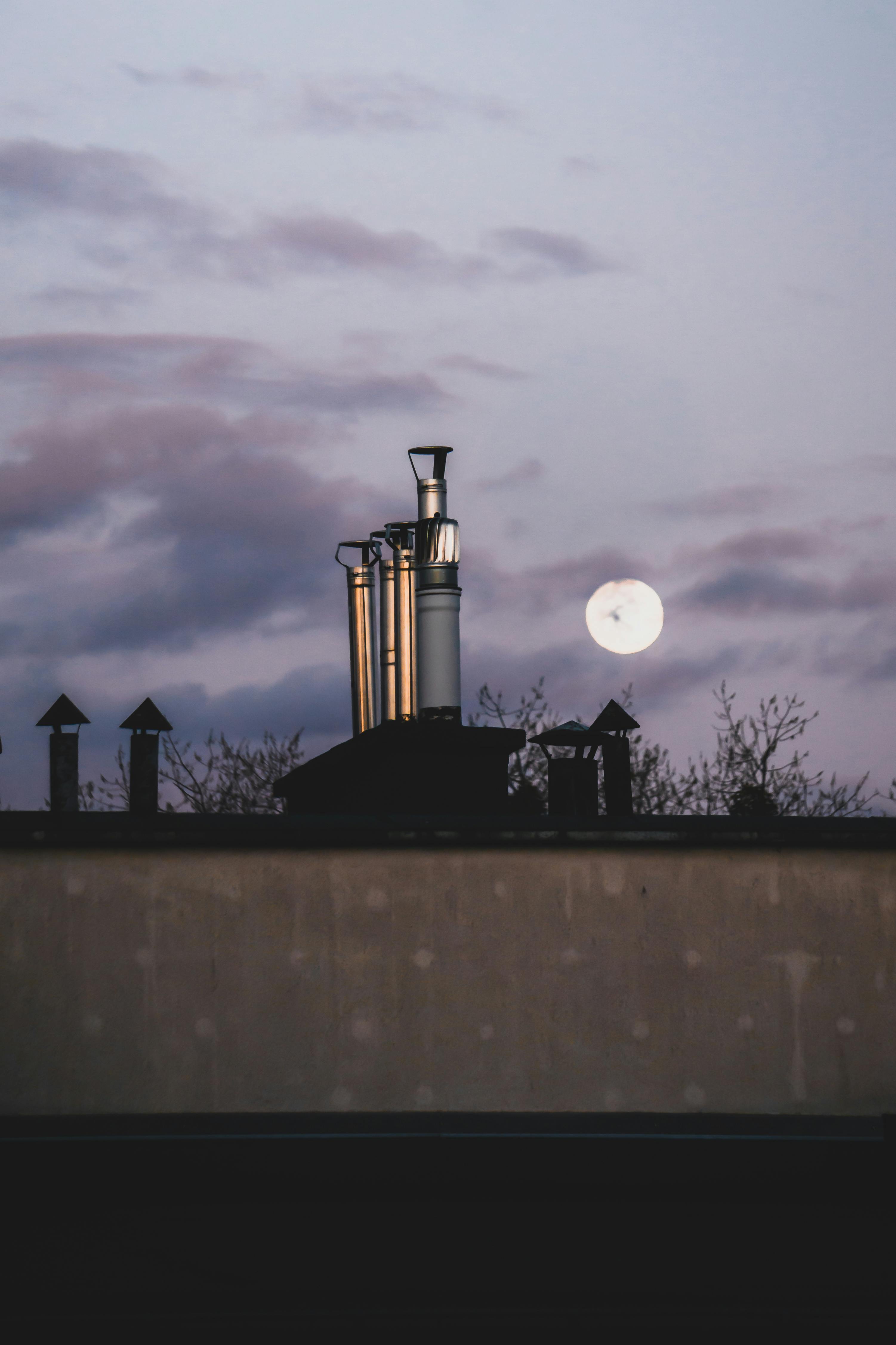 Scenic view of Torun rooftop featuring chimneys against a twilight sky with the moon.