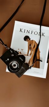 A vintage camera lays on a Kinfolk magazine against a brown background, evoking a minimalist aesthetic.