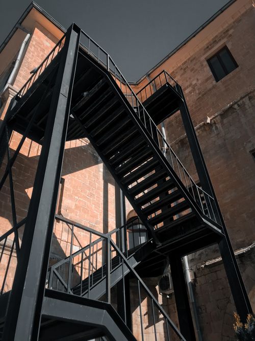 Free Low-angle shot of a black metal staircase attached to a brick building, showcasing industrial architecture. Stock Photo