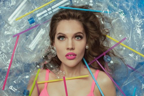 Free Conceptual portrait of a woman lying among plastic bottles and straws, emphasizing pollution. Stock Photo