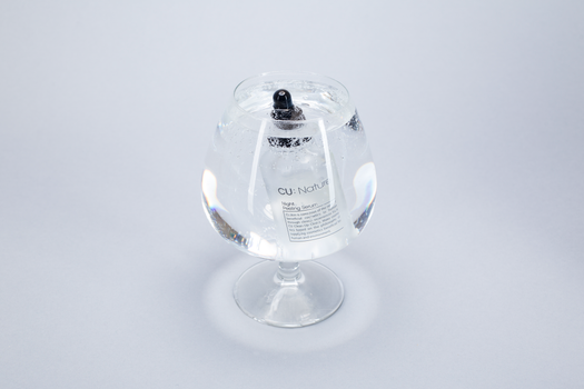 A serum bottle submerged in a wine glass filled with water, highlighting purity and clarity.